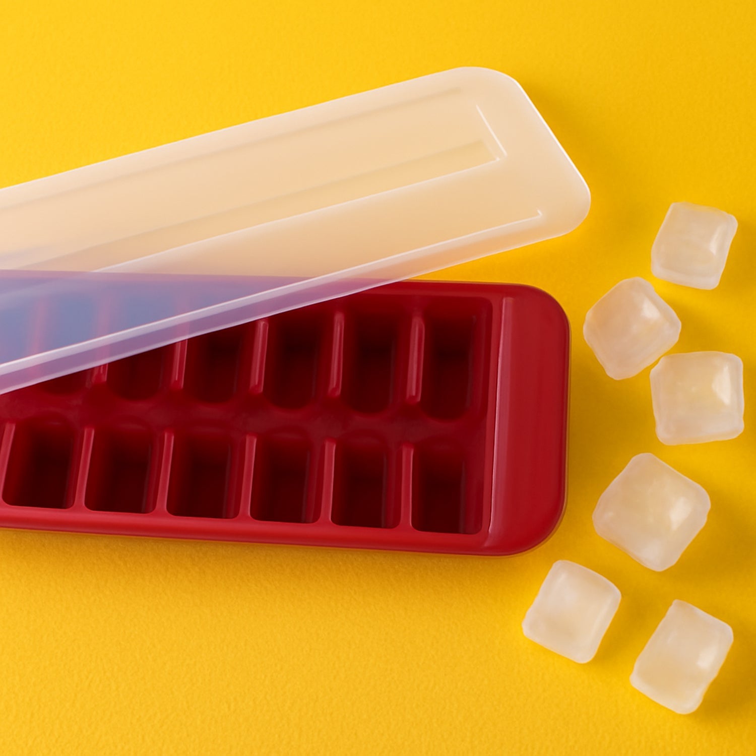 Red-and-transparent ice tray with lid partially open and several ice cubes beside it