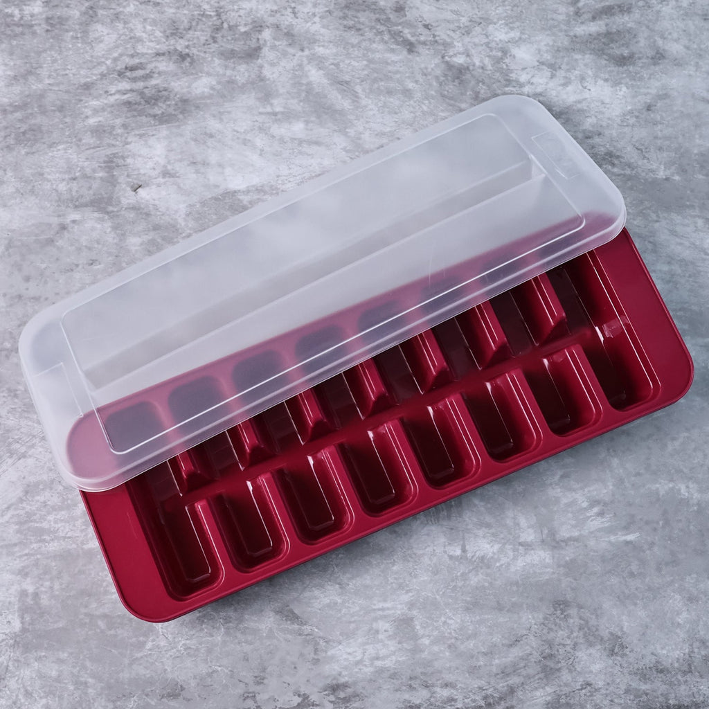 Red ice cube tray with clear lid on a gray surface, showing molded cavity rows