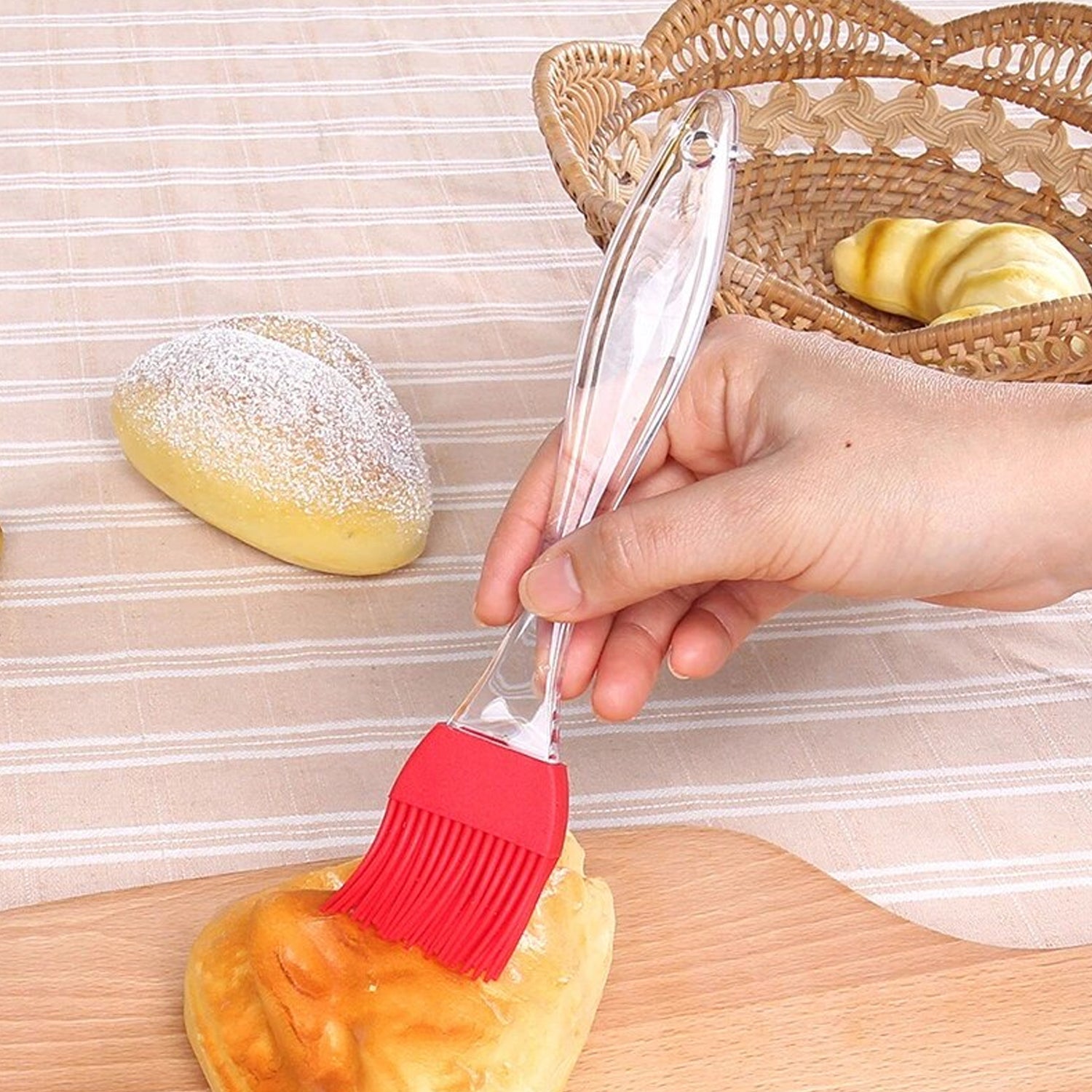 Silicone pastry brush with red bristles applying glaze to a small bun on board