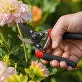 Flower pruning shear with red-and-black handles, steel blade, held near pink blossoms