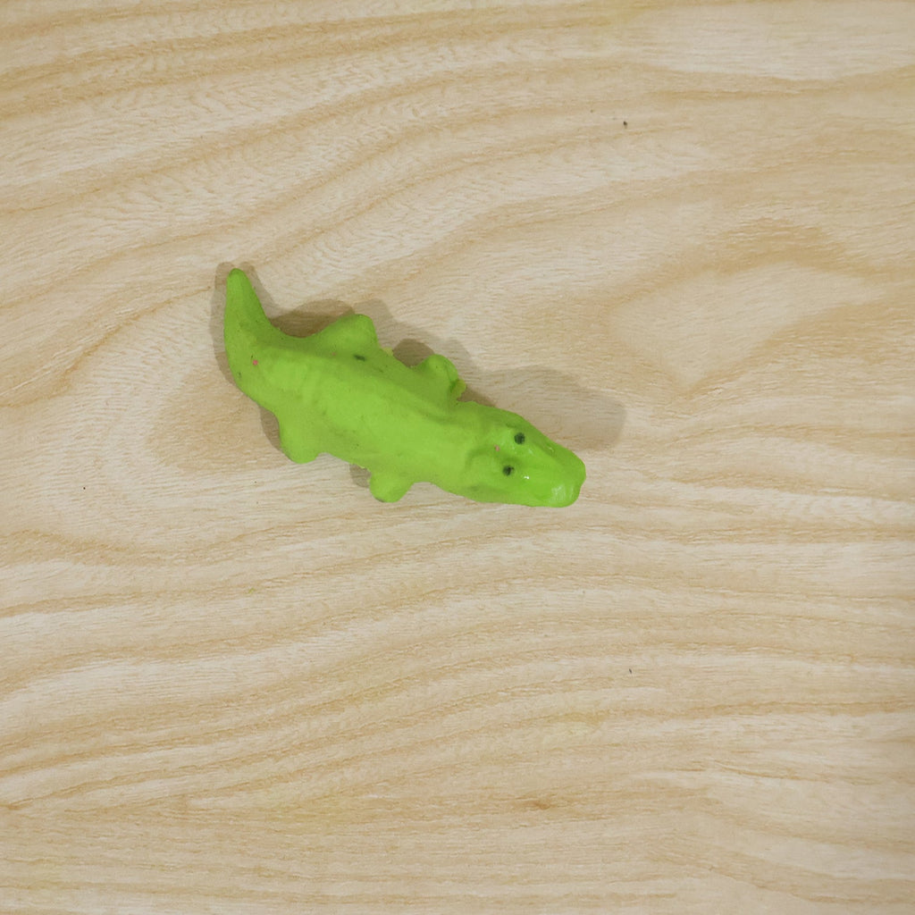 Green crocodile-shaped eraser lying on a wooden surface
