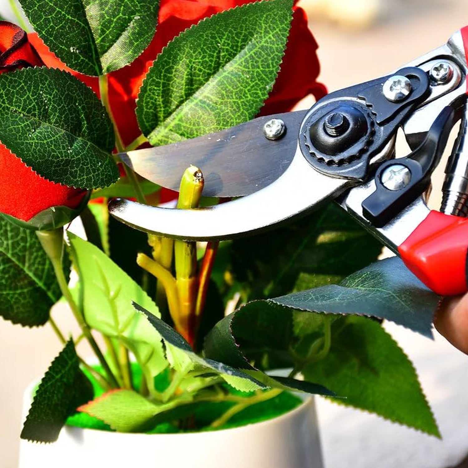 Bypass pruner cutting through green leaves with a red and black handle