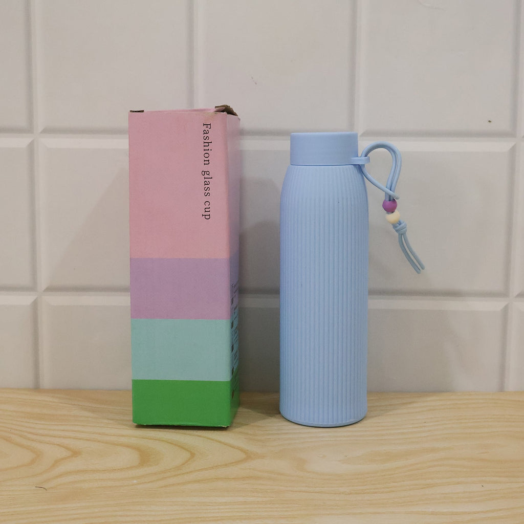 Light blue ribbed glass water bottle with silicone lid and carry loop beside product box