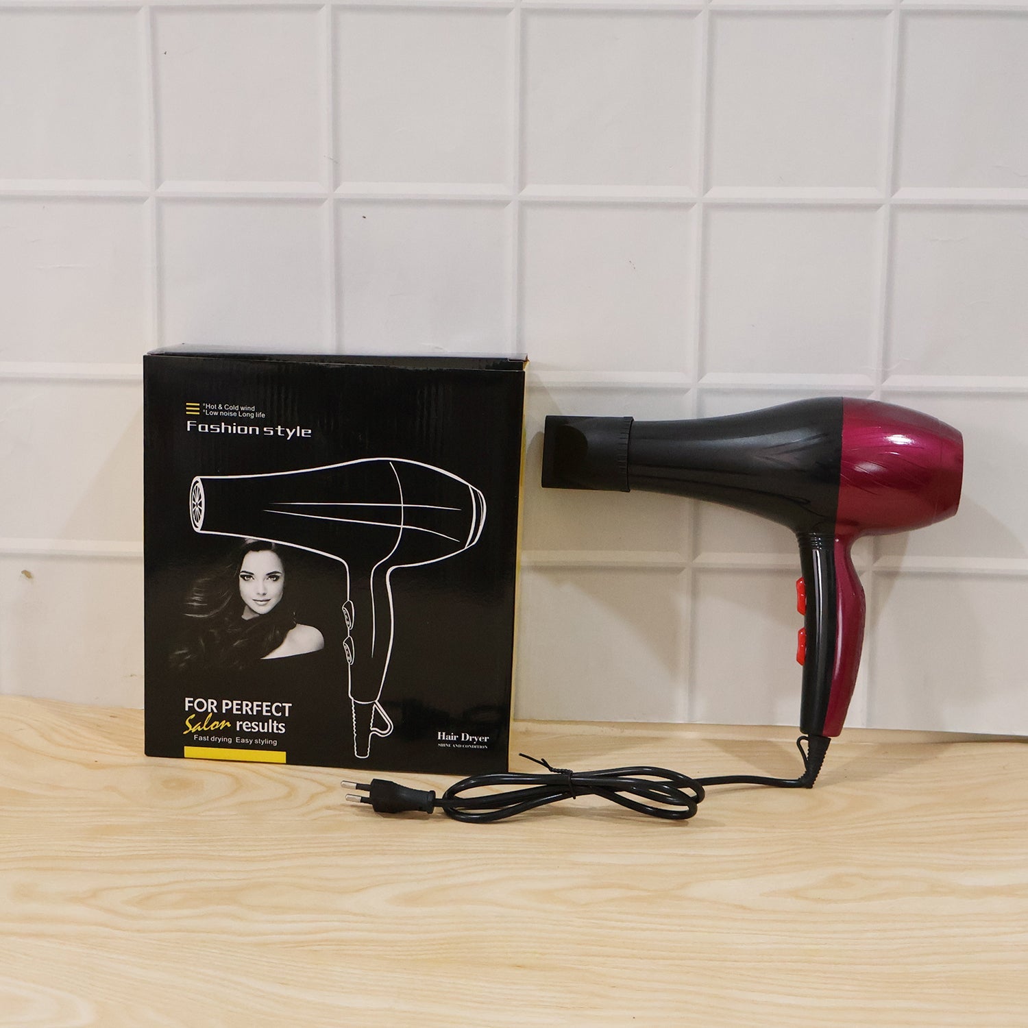 Black and burgundy hair dryer with box and power cord on wood surface