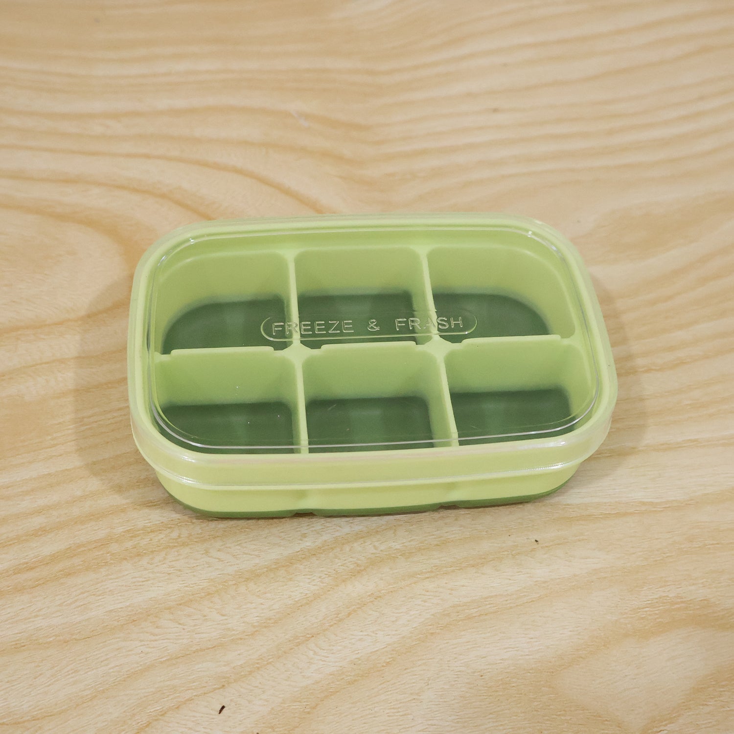 Light green 6-cavity ice cube tray with transparent lid on a wooden surface