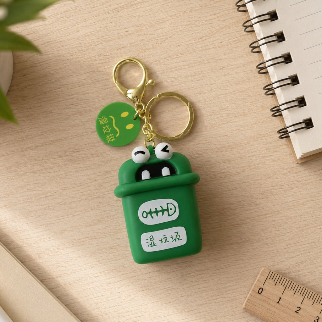 Green mini trash can keychain charm with cartoon face, gold rings and chain on wood