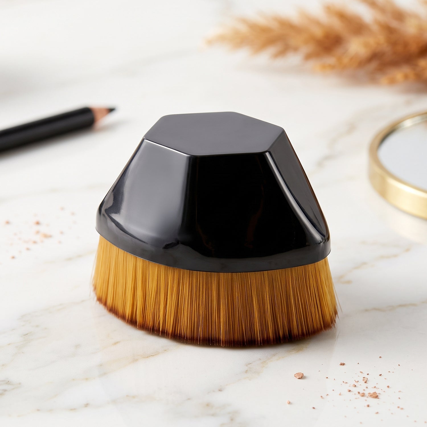 Foundation makeup brush with golden bristles and black dome base on marble surface