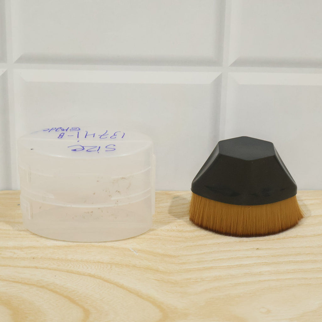 Foundation makeup brush with golden bristles and black dome base beside white container