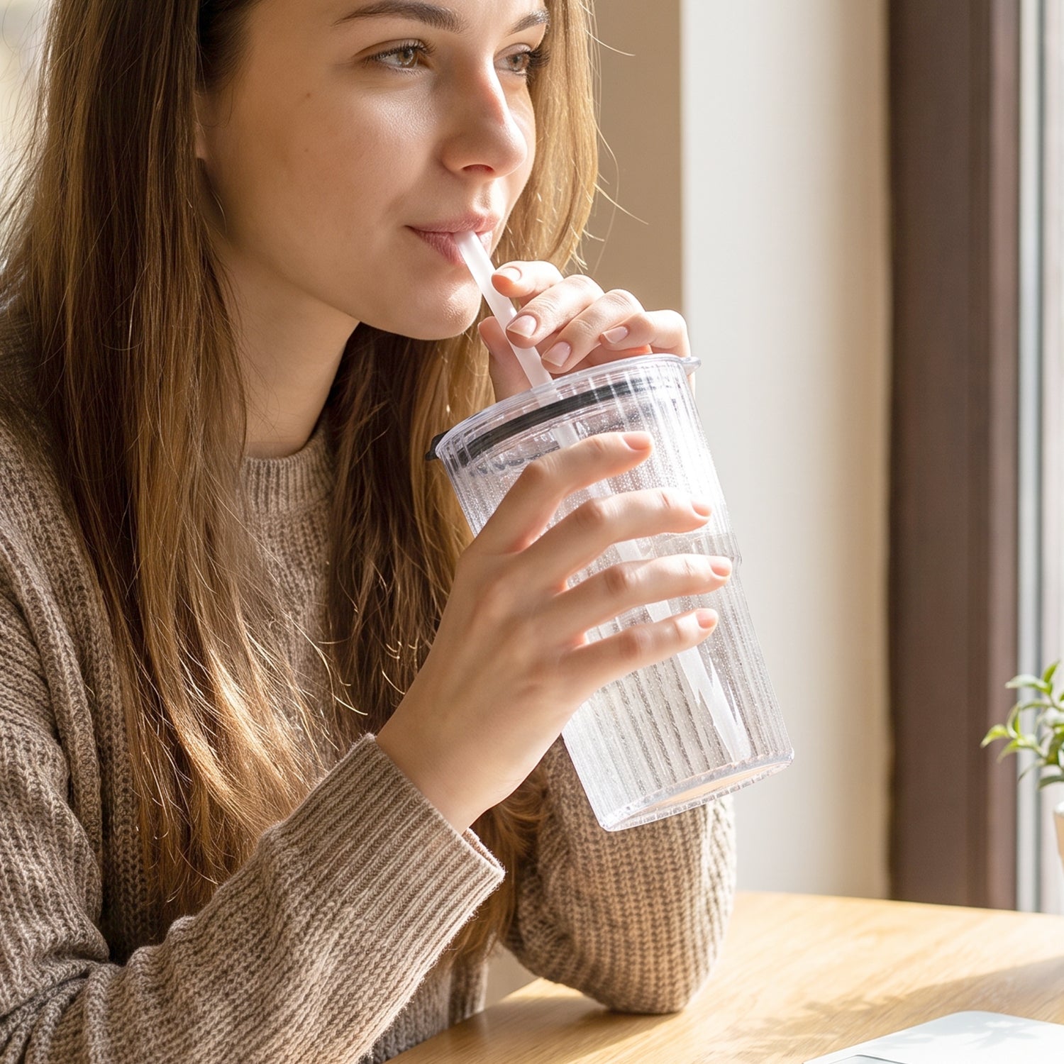 Clear plastic tumbler with lid and straw in hand, reusable drink cup