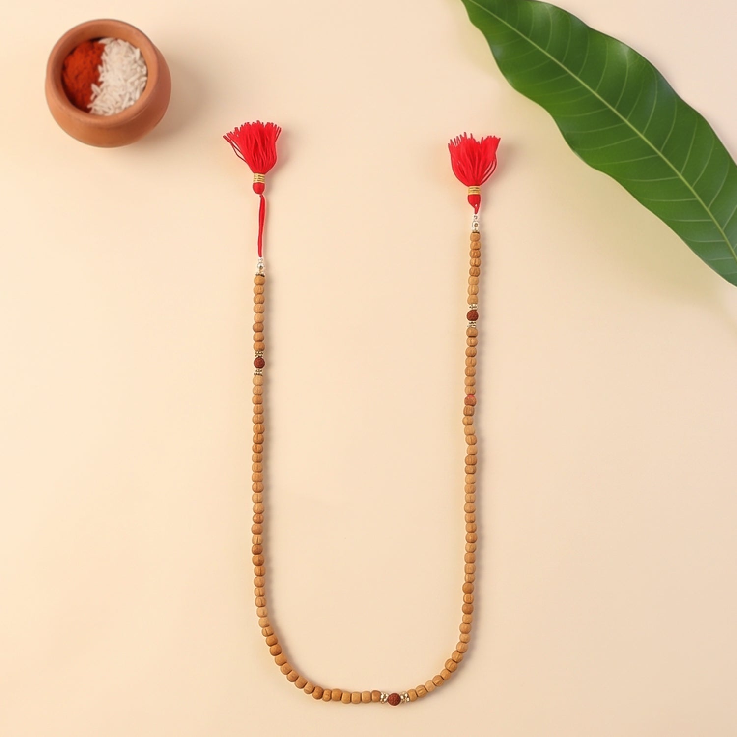 Light-wood sandalwood mala strand with red tassel ends and small central bead accents