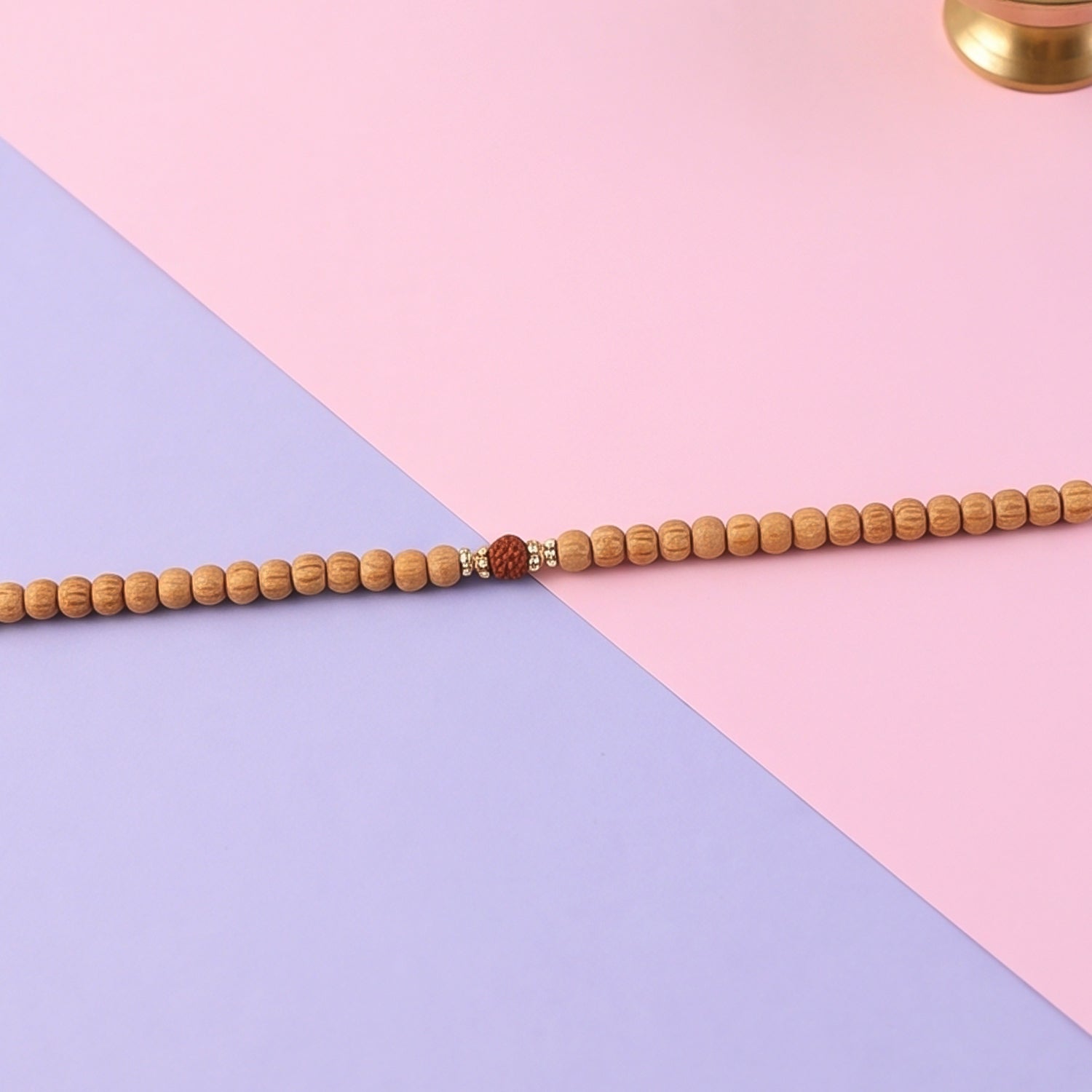 Close-up of sandalwood mala beads with small red accent bead at center and tassel ties