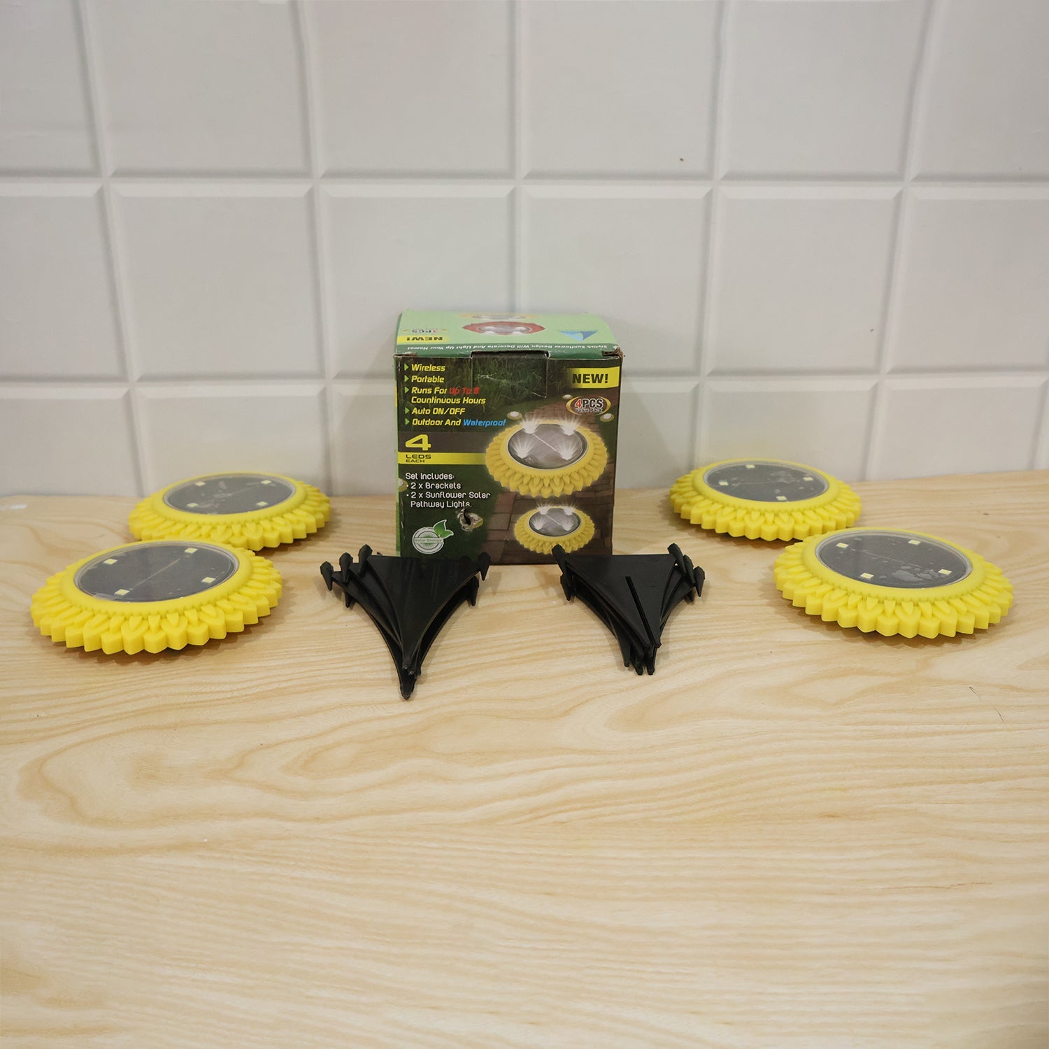 Four sunflower solar lights with black stakes and retail box on a wooden surface