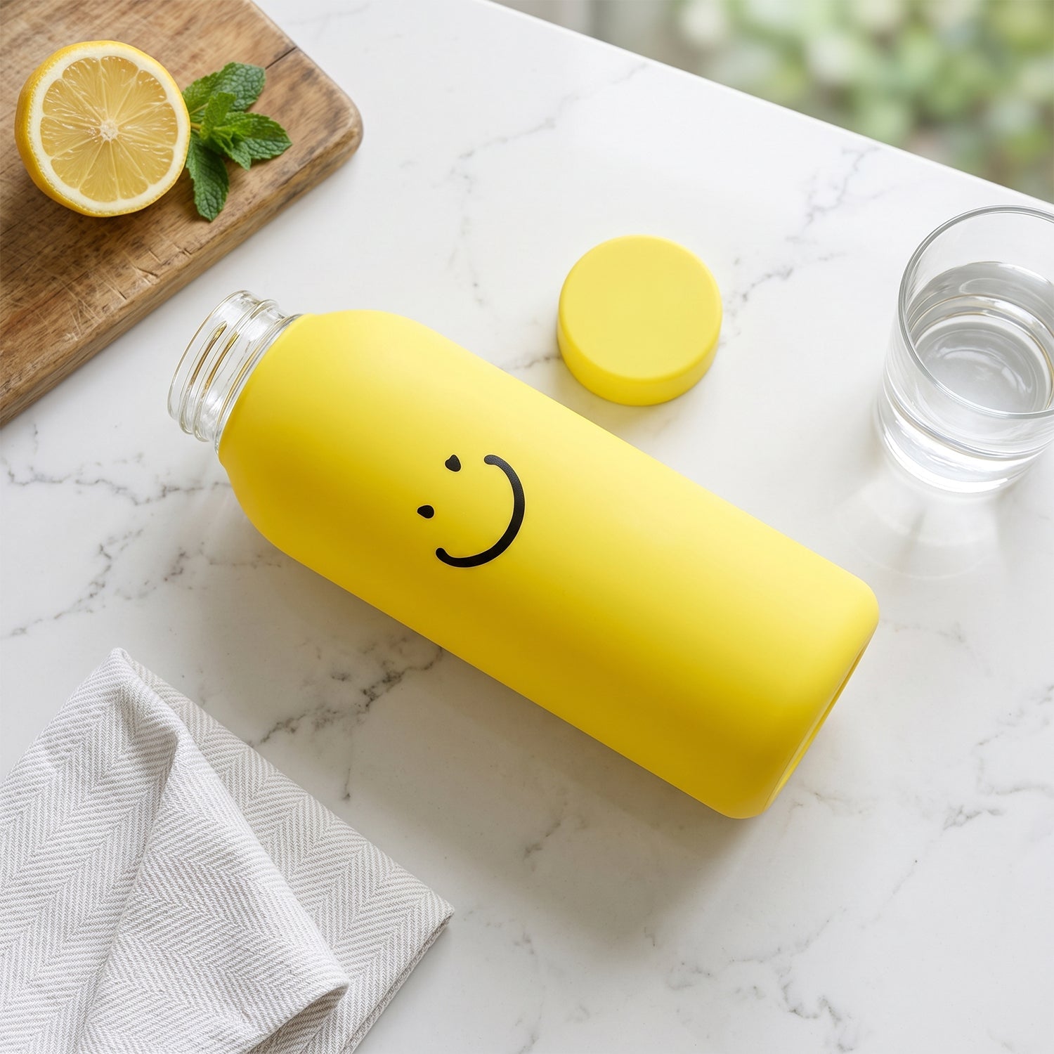 Yellow glass water bottle with silicone sleeve, smiley face, and matching cap