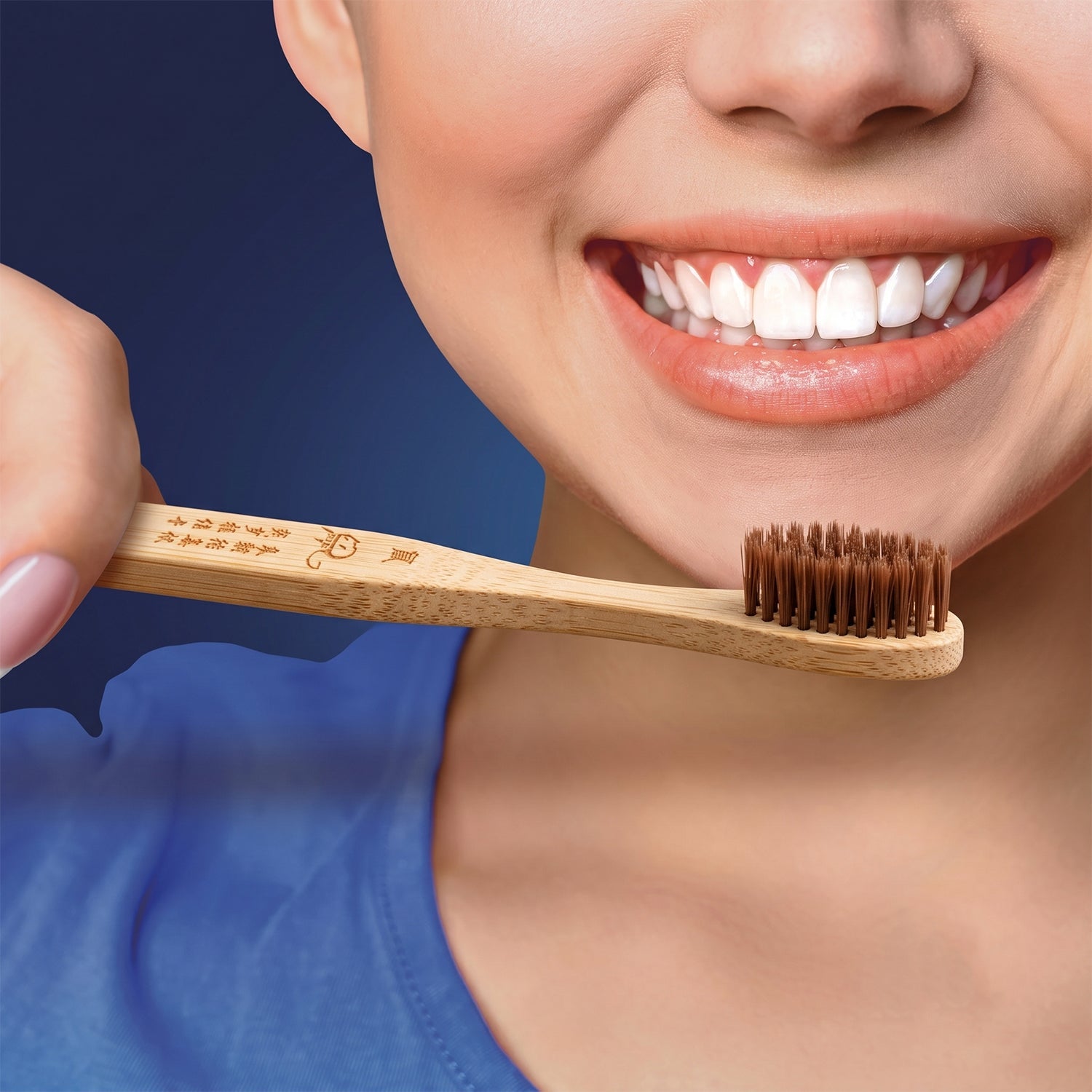Bamboo toothbrush with soft brown bristles and engraved handle held near smiling mouth