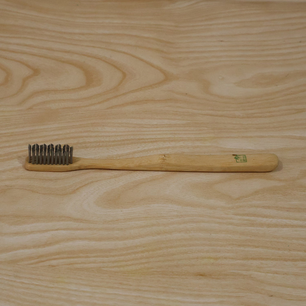 Bamboo toothbrush with soft gray bristles on light wood handle, overhead view